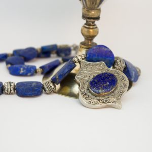 Die Kette ist aus oval förmigem Lapislazuli, unterschiedlich groß kombiniert mit silber farbenen Zwischenelemente. In der Mitte ein 3,5 x 5 cm großer Anhänger aus Alpaka und Lapislazuli. Diese Kette hat einen Karabinenverschluss.