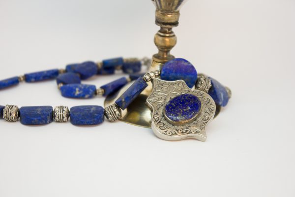 Die Kette ist aus oval förmigem Lapislazuli, unterschiedlich groß kombiniert mit silber farbenen Zwischenelemente. In der Mitte ein 3,5 x 5 cm großer Anhänger aus Alpaka und Lapislazuli. Diese Kette hat einen Karabinenverschluss.